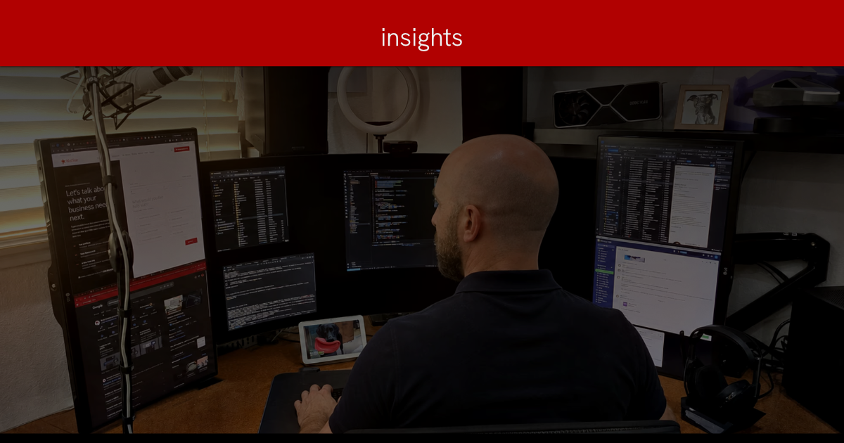 A bald, bearded man, Mike Johnstone President of InfoStar, in a dark polo sits at a corner desk working across five monitors showing code, email, and web pages, with a podcast microphone and ring light nearby.